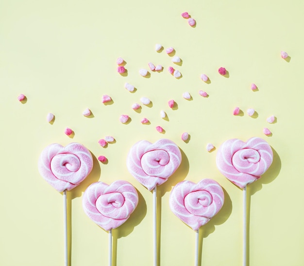 Pink lollipops in the shape of hearts with color sugar on a yellow background Top view and copy space