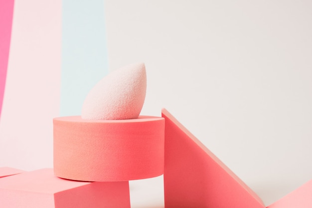 Pink makeup sponge and wide brush for applying blush on geometric pads, colored background, pink background