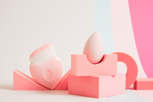 Pink makeup sponge and wide brush for applying blush on geometric pads, colored background, pink background