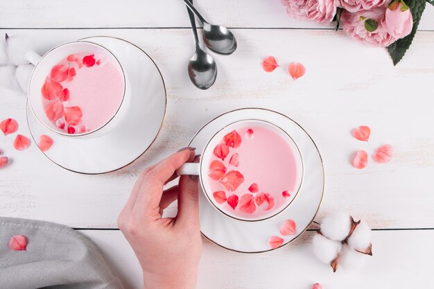 Pink matcha with rose petals on white background Female hand holds a cup with trending vegan tea