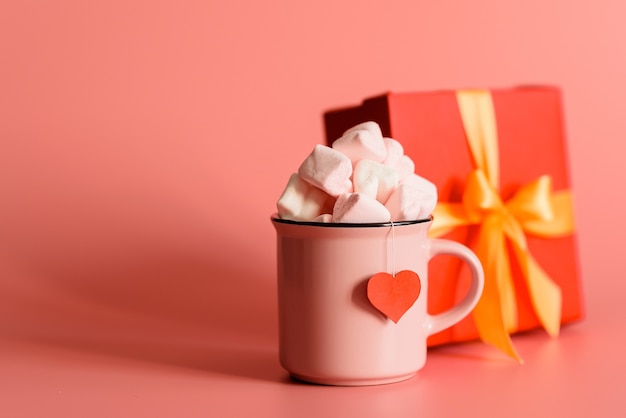 Pink mug filled with marshmallows in the form of hearts and gift box