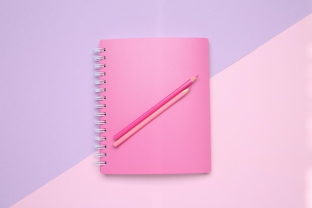 Pink notebook and pencils on color background top view