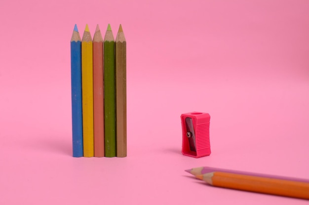 Pink pencil sharpener with several kinds of colored pencils on a pink background