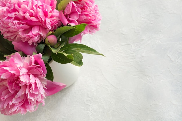 Pink peony flowers in vase on grey. Top view.