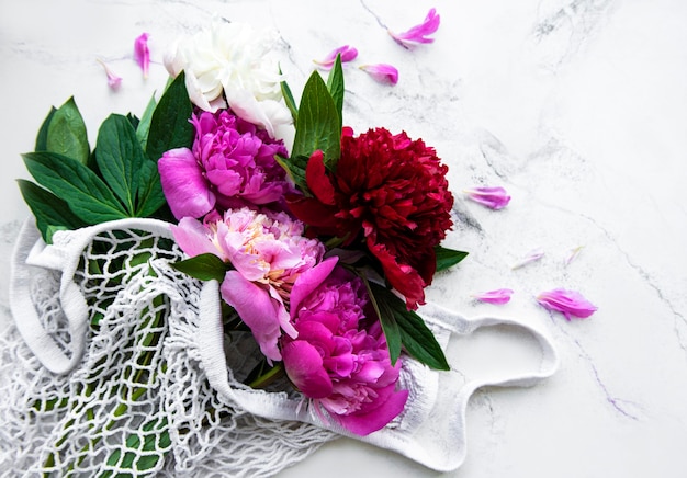 Pink peony in string bag  on white marble surface