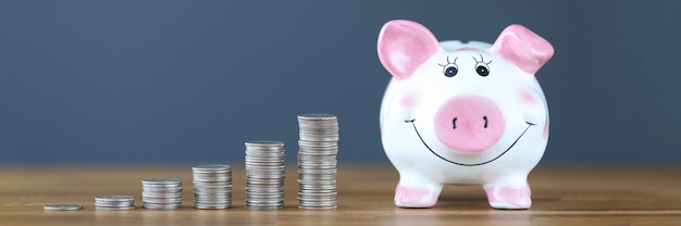 Pink piggy bank standing on table near heaps of coins business investment concept