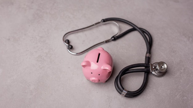 Pink piggy bank and stethoscope on a gray background Concept of how to save on health