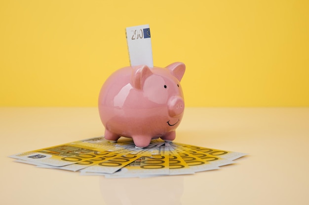 Pink piggy bank with euro banknotes on yellow background