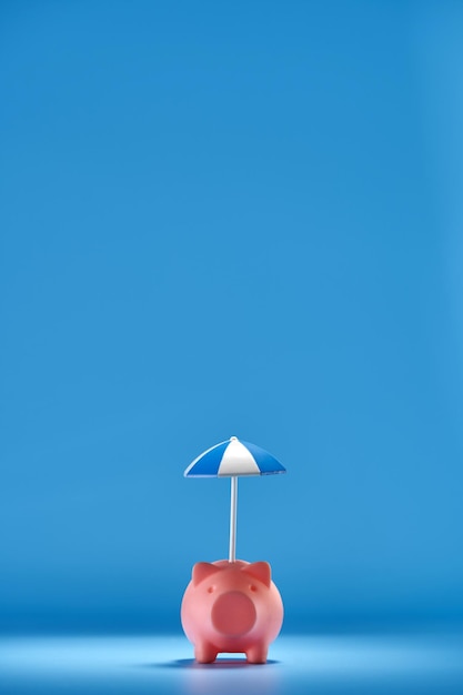 Pink piggy bank with small umbrella against blue background