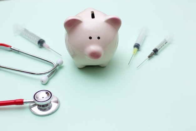 Pink piggy bank with stethoscope and syringe on green background