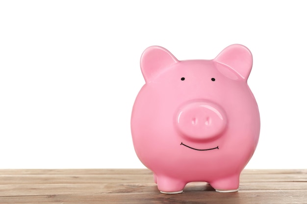 Pink piggy bank on wooden table against white background