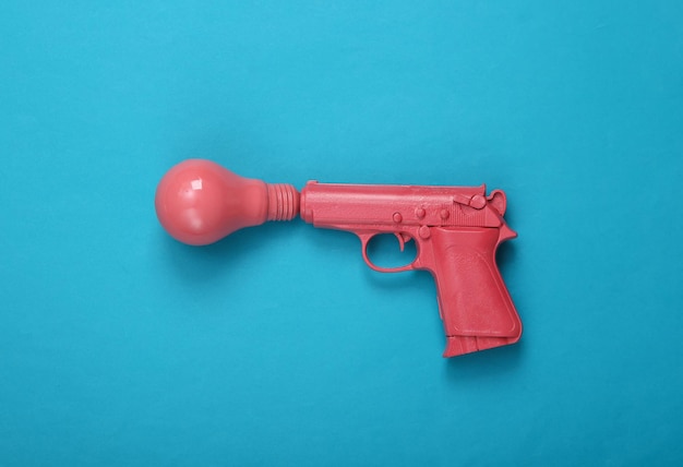 Pink pistol gun with light bulb on blue background Creative minimalism layout Fresh idea Concept art Flat lay Top view