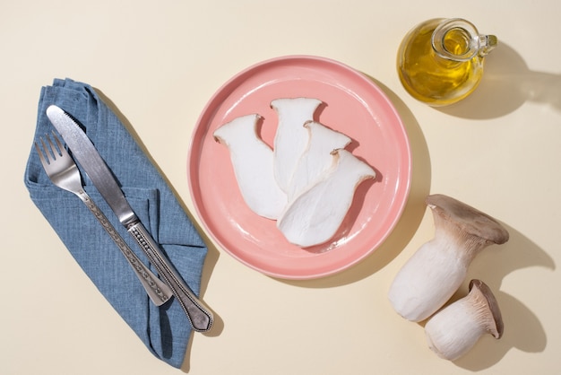 Pink plate with fresh king oyster mushrooms, rosemary sprigs, knife, fork