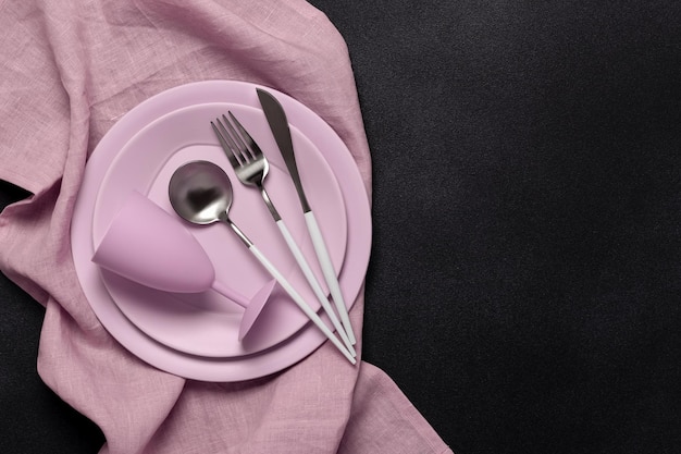 Pink plates wine glass and cutlery on a dark black background Top view Card or menu template flat design Tableware crockery Aerial view copy space Table setting Flat design