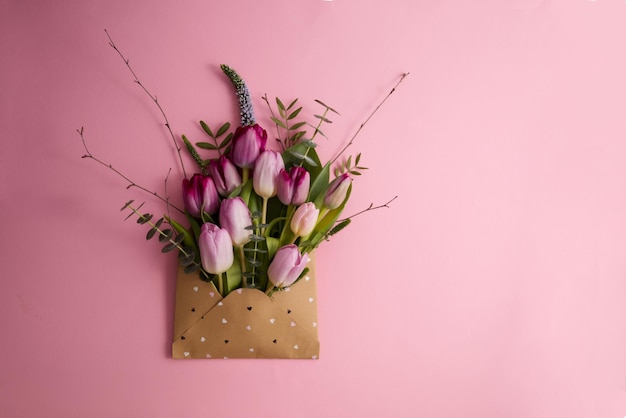 Pink and purple tulips in a paper envelope on a pink background copy space