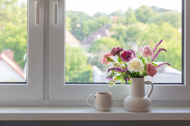 pink purple and white flowers in white jug with cup of tea on windowsill