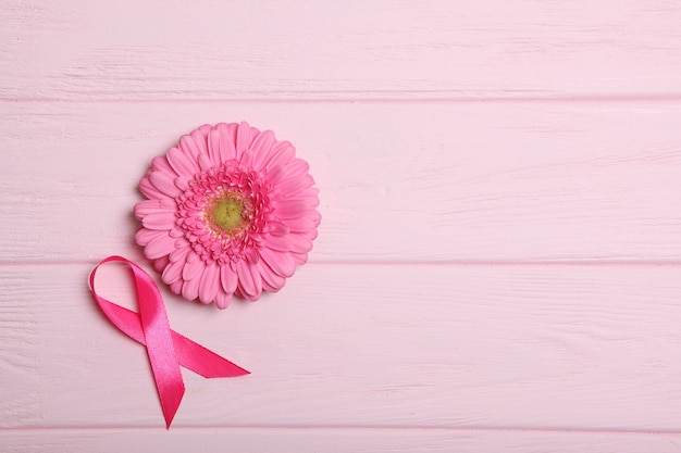 Pink ribbon gerbera and stethoscope on a colored background top view