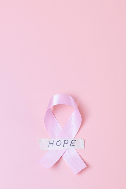 Pink ribbon with sticky tape and the word hope on a pink background