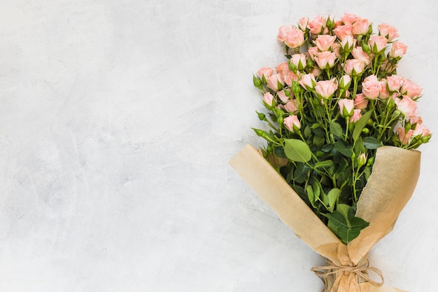 Pink roses bouquet wrapped in brown paper on concrete backdrop