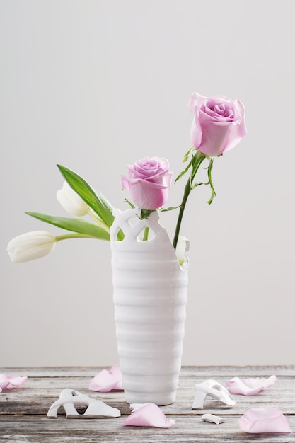 pink roses in broken vase on old wooden table