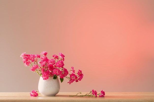 pink roses in ceramic vase on light red background