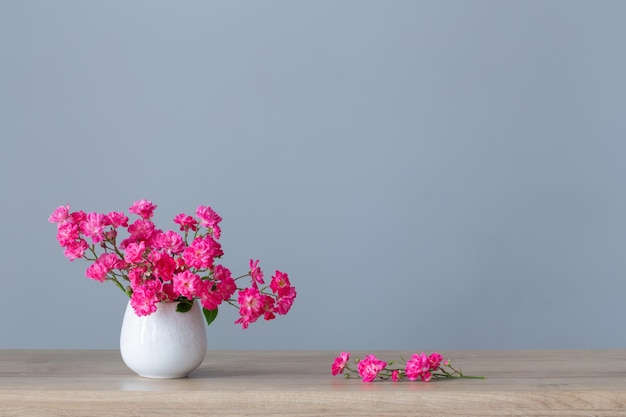 Pink roses in ceramic vase on wooden shelf