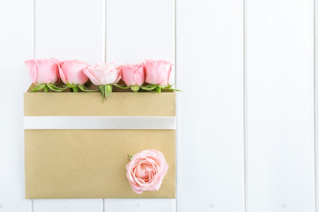 Pink roses in envelope on white wooden background.