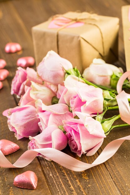 Pink roses and gift wrapped in recycled paper on rustic wood table.