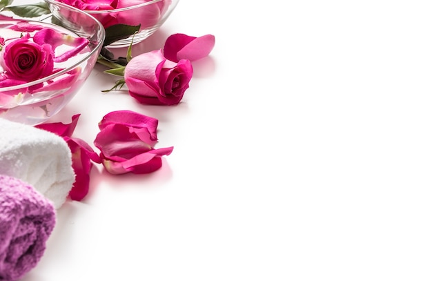 Pink roses petals in bowl with towels and pure water over white.. Spa and wellness concept.