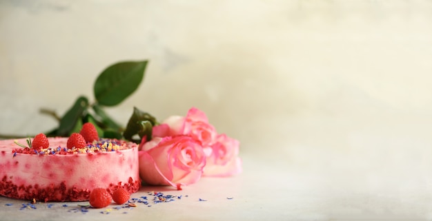 Pink roses and raspberry cake with fresh berries, rosemary, dry flowers on concrete background. 