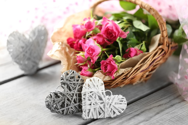 Pink roses in a wicker basket and decorative hearts on a white table close up