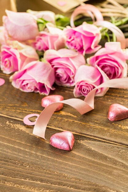 Pink roses with chocolates on rustic wood table.