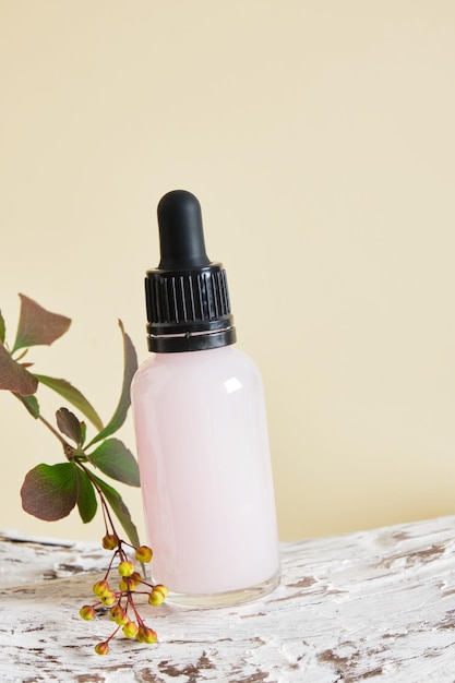 Pink serum in a transparent dropper bottle on a wooden snag beige background