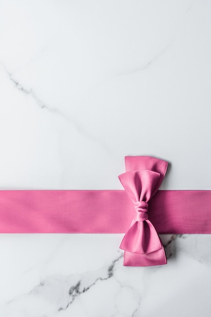 Pink silk ribbon and bow on marble background girl baby shower present and glamour fashion gift decor for luxury beauty brand holiday flatlay design