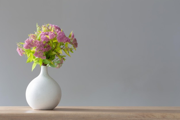 pink spirea in white vase on wooden shelf