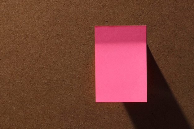 Pink square office sticky notes on cork board with hard shadow