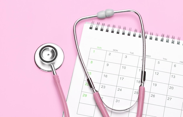 Pink stethoscope and calendar on a pink background Concept female doctor gynecologist