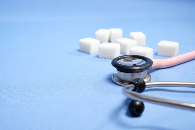 Pink stethoscope, sugar cubes on a blue space, diabetes. Space for text, selective focus