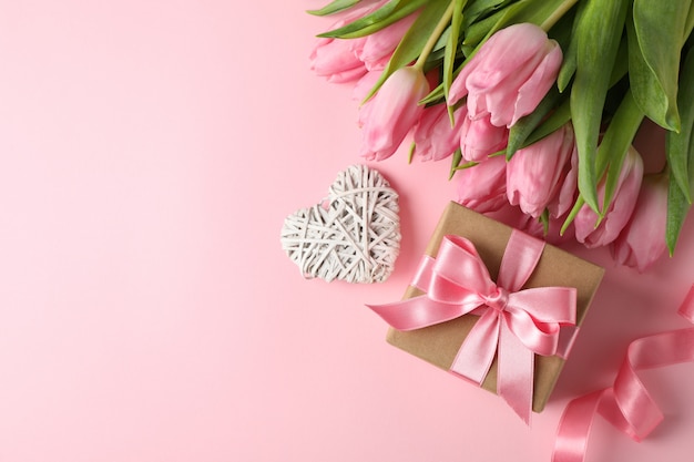 Pink tulips, gift box and decorative heart on pink, space for text