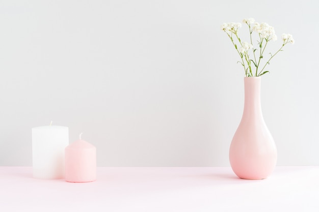 Pink vase with gypsophila and two candles on a pink table with copy space