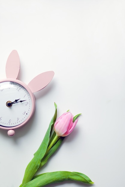 Pink vintage alarm clock with beautiful tulip flower top view selective focus on white background