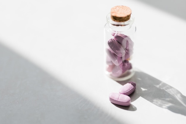 Pink vitamin pills in a glass jar jn white table. Conservative medicine. Health care concept.