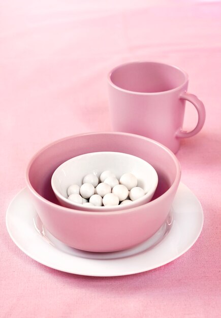 Pink and white crockery with sugar dragees inside on a pink cloth surface