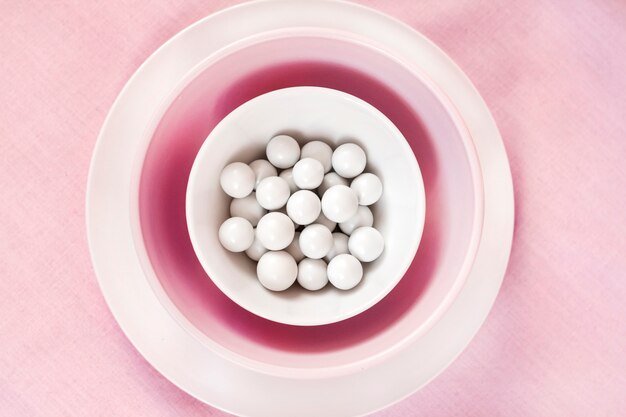 Pink and white crockery with white round sugar dragees inside on a gentle pink cloth background