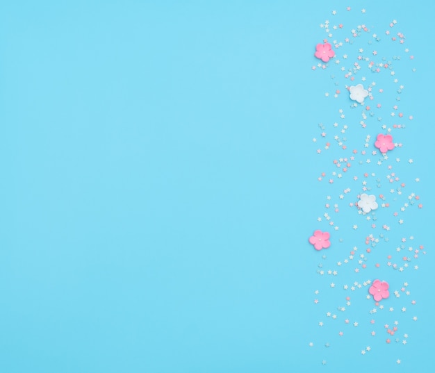 Pink and white flowers made of foamiran with star shaped confetti on blue background.