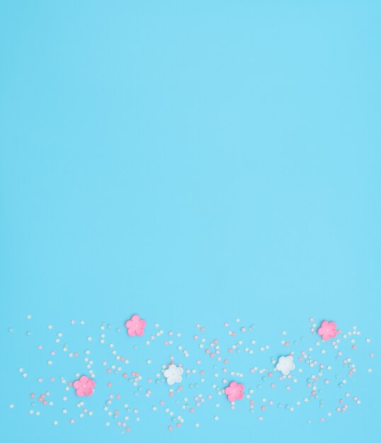 Pink and white flowers made of foamiran with star shaped confetti on blue.