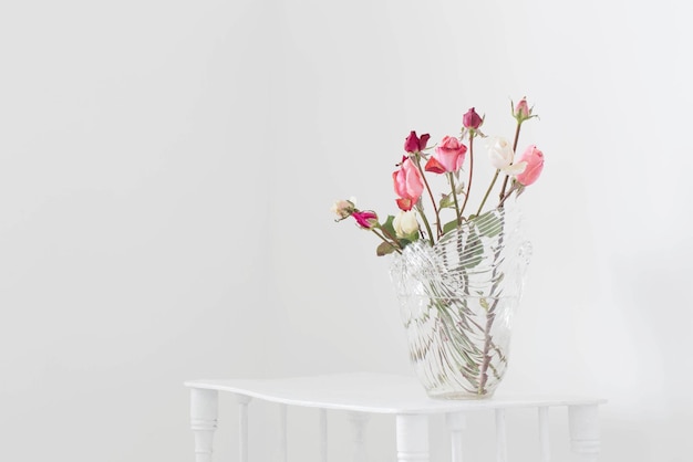 Pink and white roses on glass vase on white wooden shelf