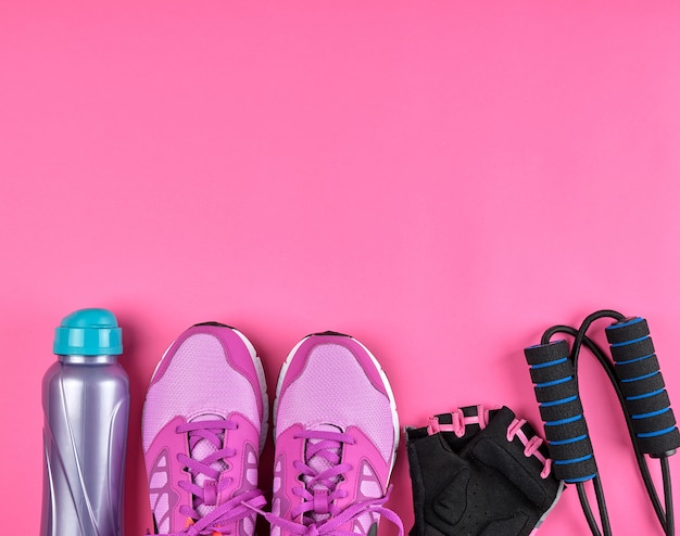 Pink women's sneakers, a bottle of water, gloves and a jump rope for sports 