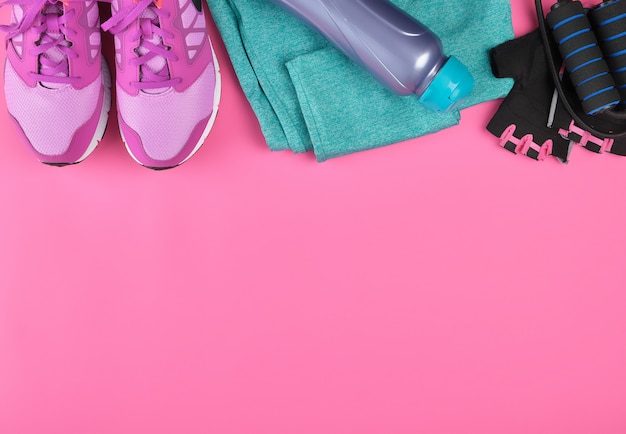 Pink women's sneakers, a bottle of water, gloves and a jump rope for sports 