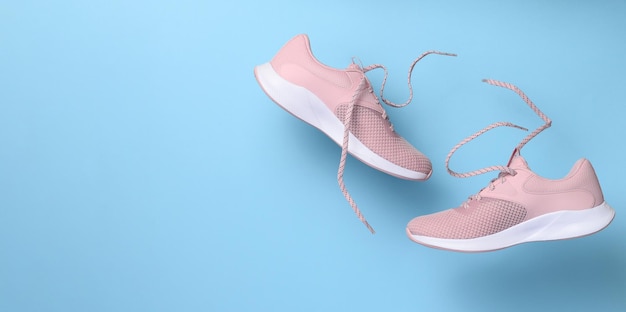 Pink women's sports sneakers with laces levitate on a blue background